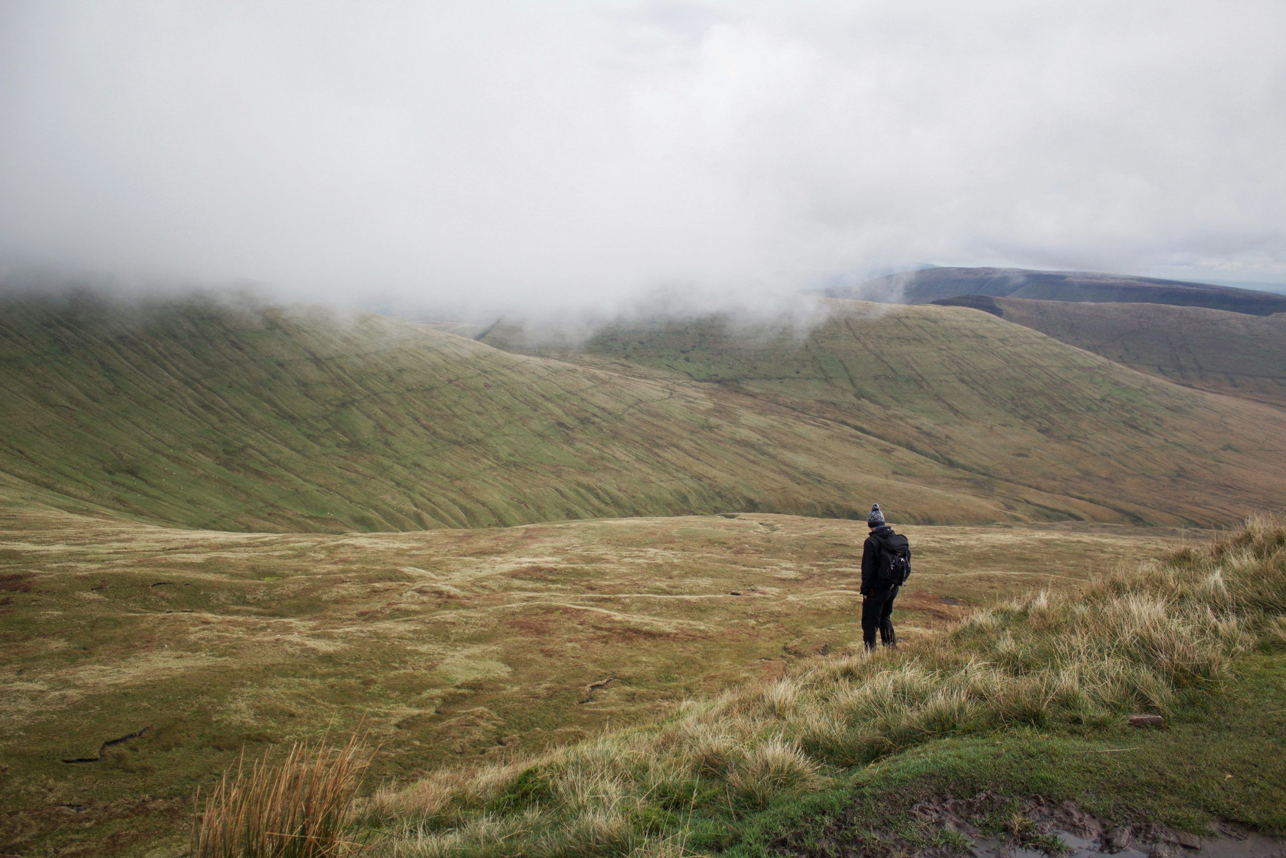 Traveler wearing modular rainwear while hiking through Scottish highlands during heavy rainfall